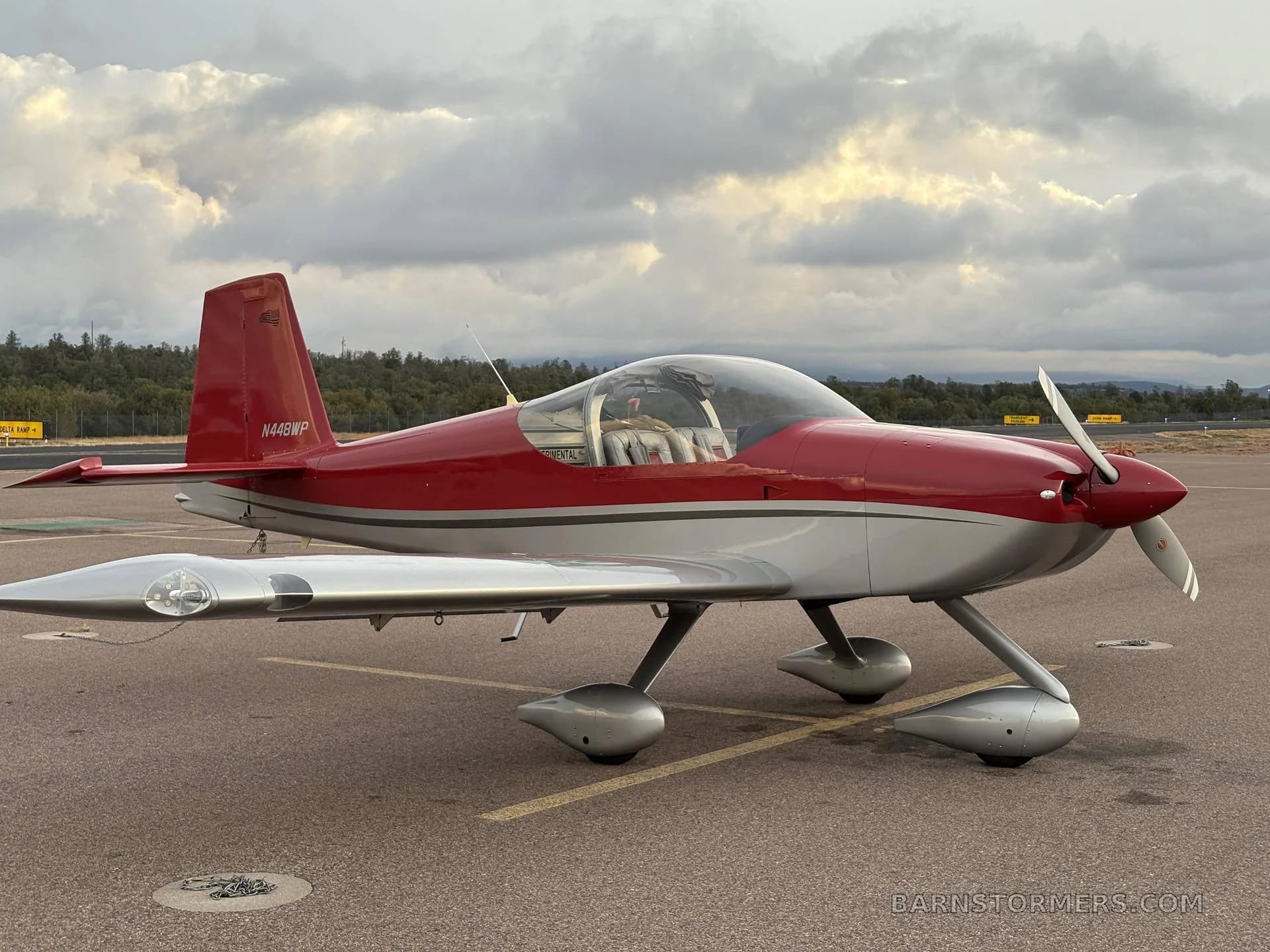 A red and silver single-engine aircraft, N448WP, parked on an asphalt ramp under a cloudy sky.