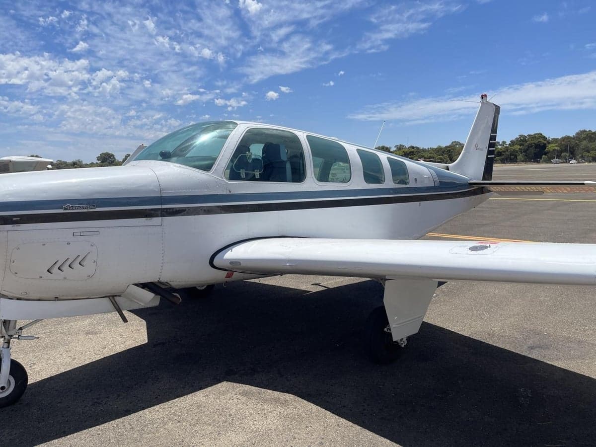 A white and blue Beechcraft Baron aircraft parked on an asphalt tarmac under a blue sky.