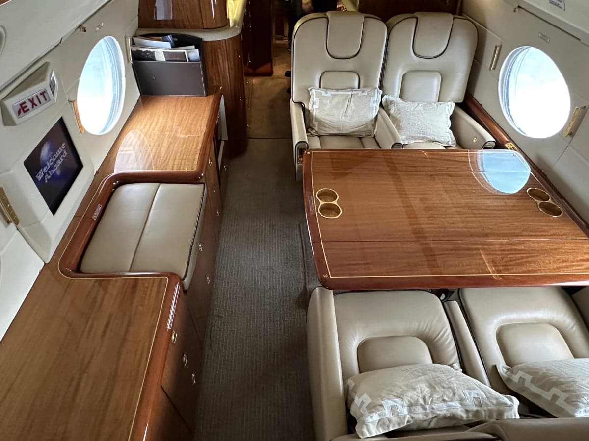 A view of the aircraft interior showing the leather seats, wooden tables, and cabinets.