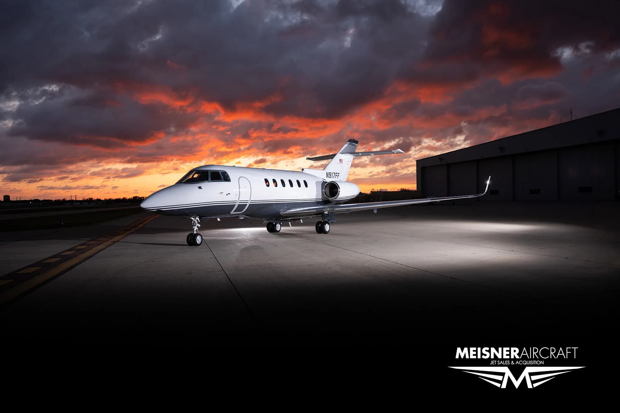 A white and grey business jet (N917FF) parked on a tarmac with a hangar in the background at sunset.