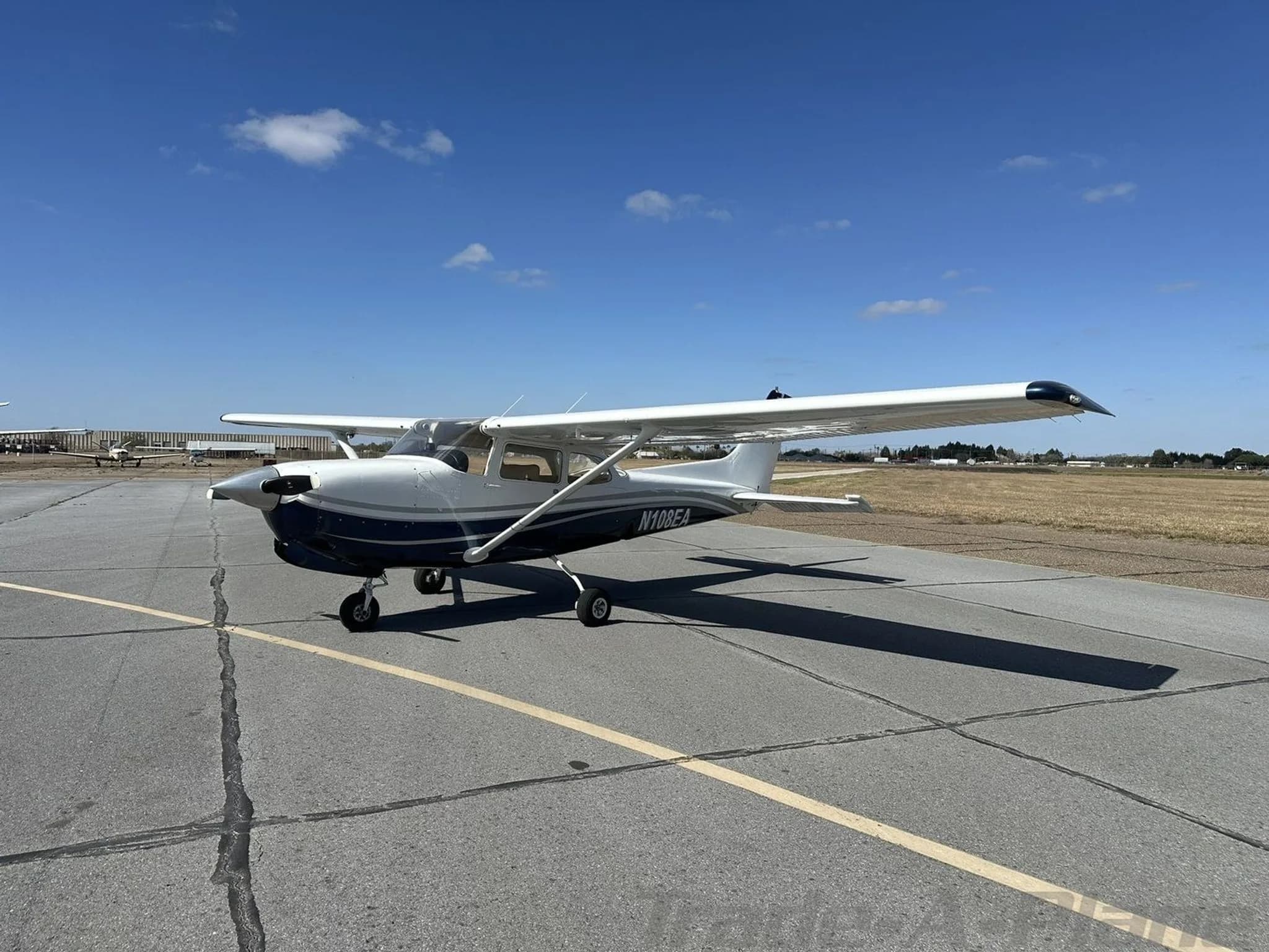 Side view of a white and dark blue Cessna N108EA aircraft parked on an airport tarmac.