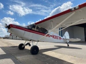 Piper Cub aircraft with red and white paint scheme parked on the tarmac.