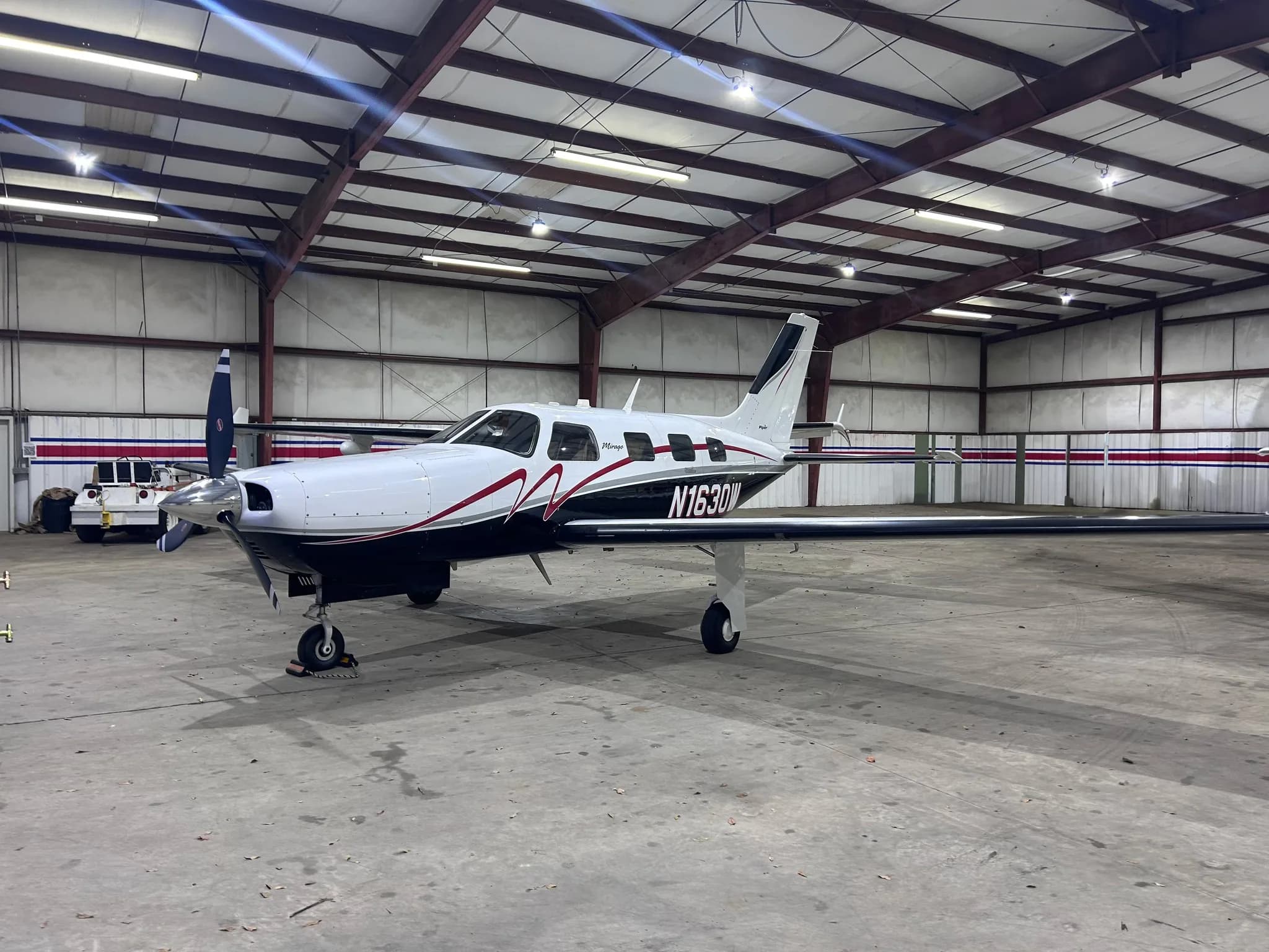 A white and black Piper Mirage aircraft with red accents, registration N1630W, parked inside a hangar.