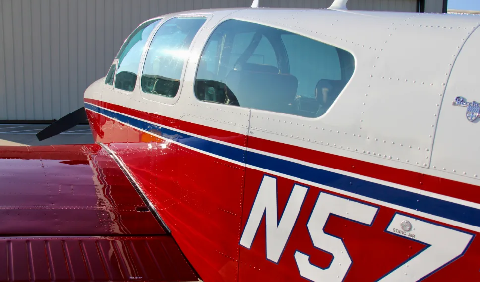 A close-up view of the cockpit windows and red fuselage of a Beechcraft Bonanza N5724V.