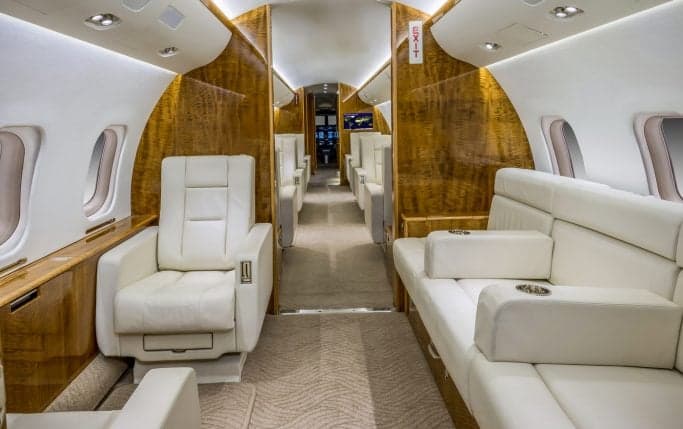 Aircraft interior featuring a white leather couch and wood paneling.