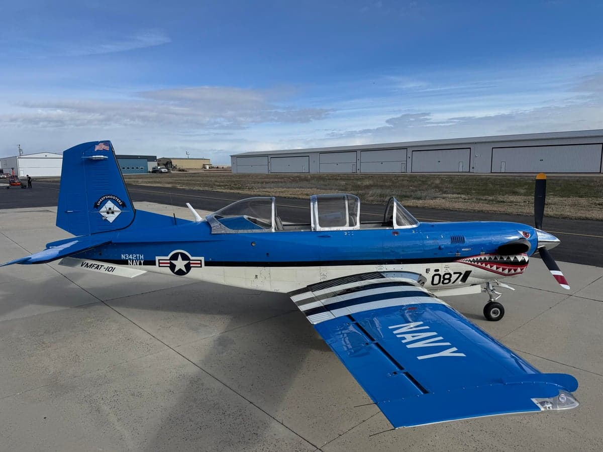 A blue and white SIAI-Marchetti SF.260 is parked on the tarmac with a shark mouth paint scheme.