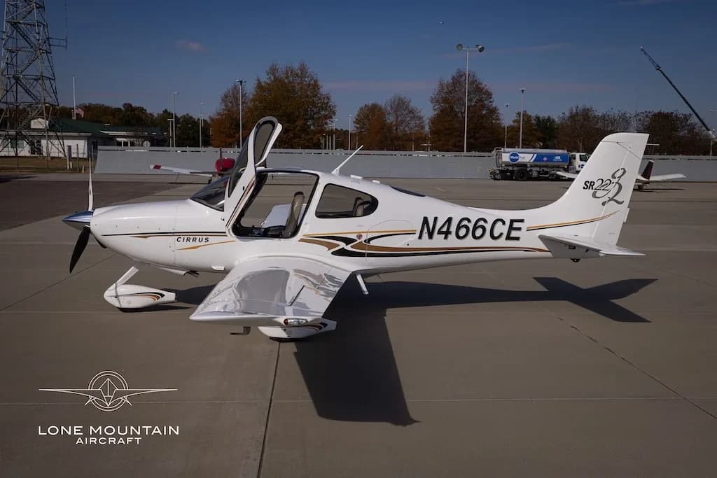 A white Cirrus SR22 aircraft with gold and black stripes, registration N466CE, parked on an airfield with its doors open, viewed from the right side.
