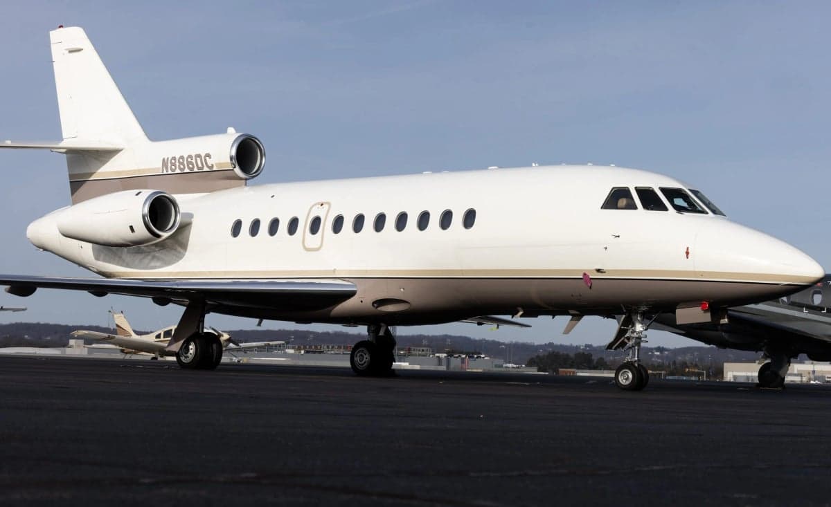 A Dassault Falcon 900EX with a white and tan paint scheme parked on the tarmac.
