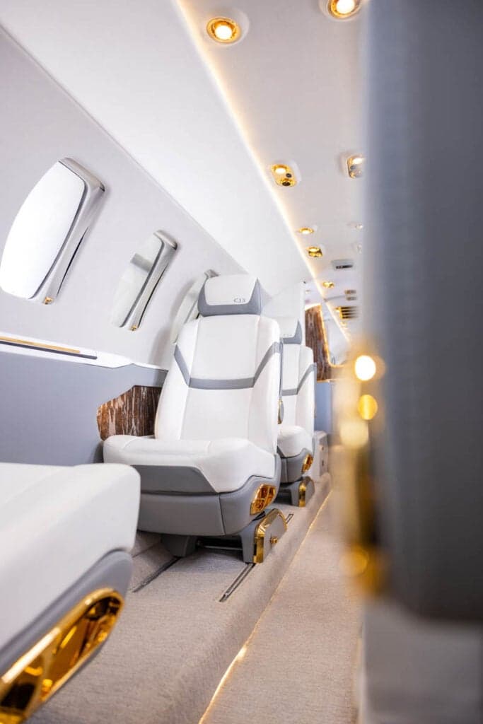 A view of the Citation CJ3 cabin interior with white leather seats and gold accents.