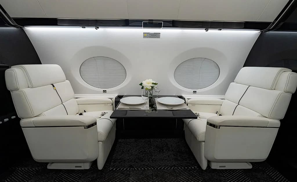 Two white leather seats in the business jet cabin with a small table set for dining between them.