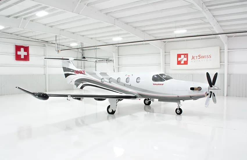 A close-up view of the front fuselage of a white Pilatus PC-12NG aircraft with "PILATUS" in red text and gray and red stripes.