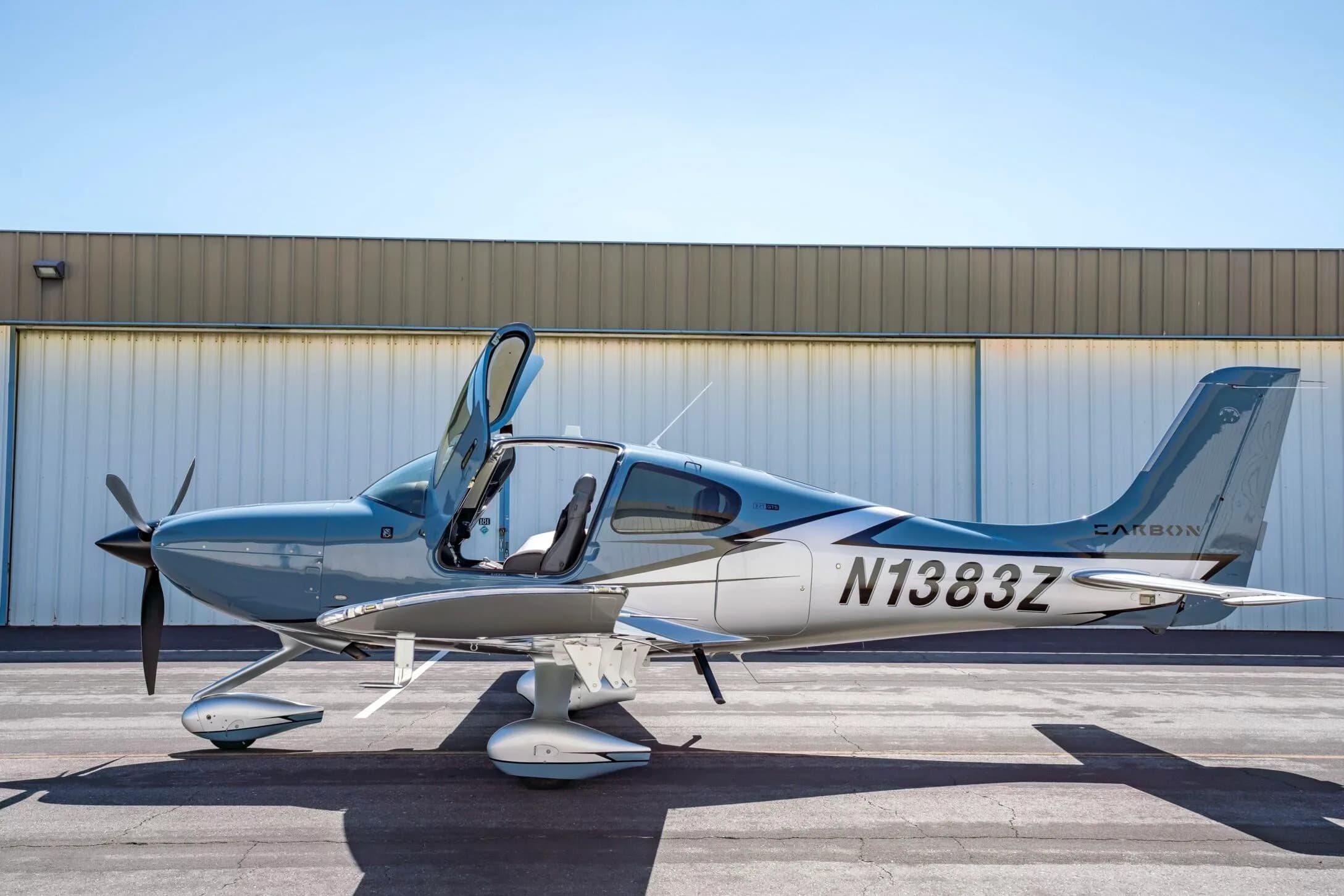 A light blue and silver Cirrus SR22T aircraft, N1383Z, with its doors open, parked on an tarmac.
