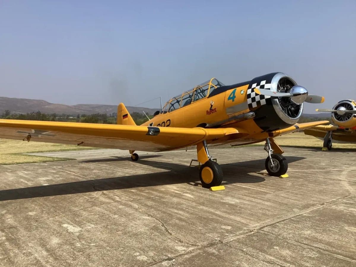 A yellow T-6 Texan aircraft with a checkered nose sits on the tarmac.