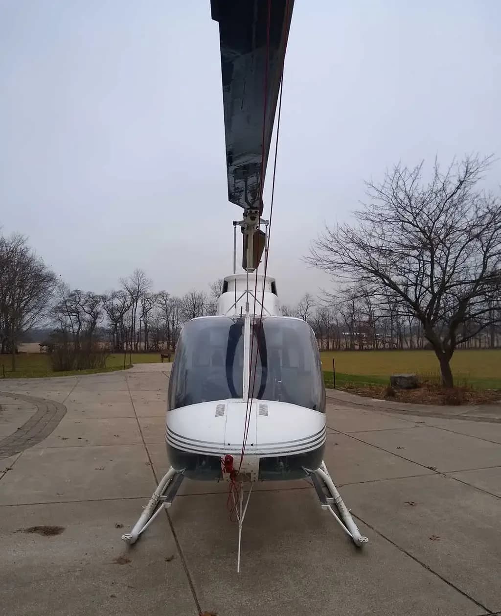 Front view of a white helicopter with dark grey stripes on a concrete driveway.