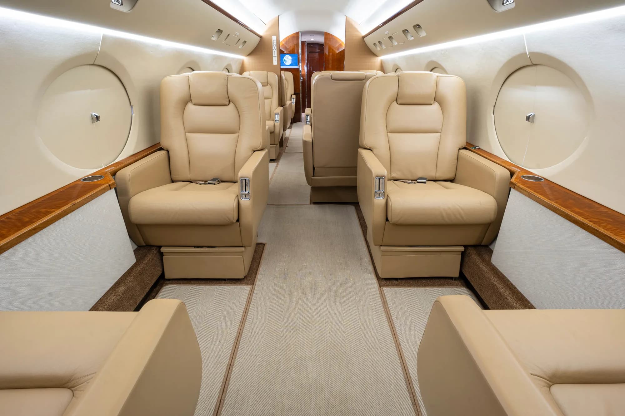 The luxurious beige leather interior cabin of a business jet with an aisle.