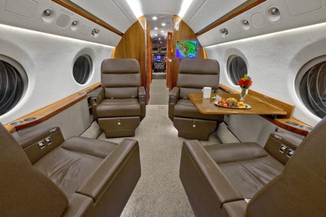 View of the aircraft interior with leather seats and a table set for a meal.