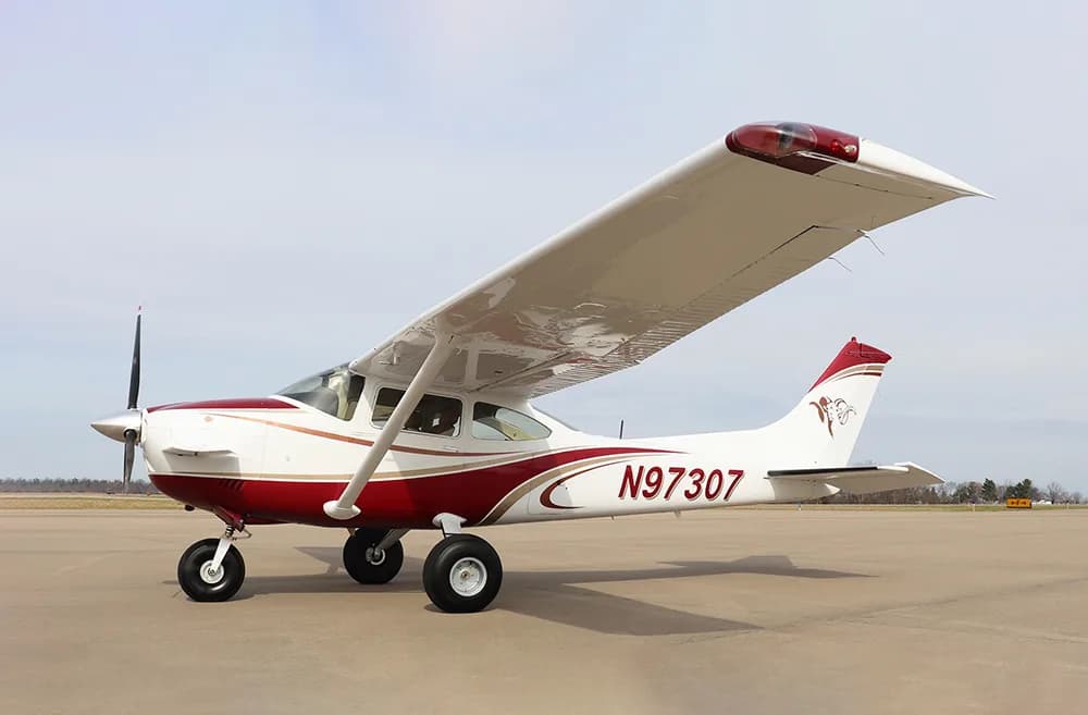 A side view of a white and red single-engine high-wing aircraft, N97307, parked on an airfield.