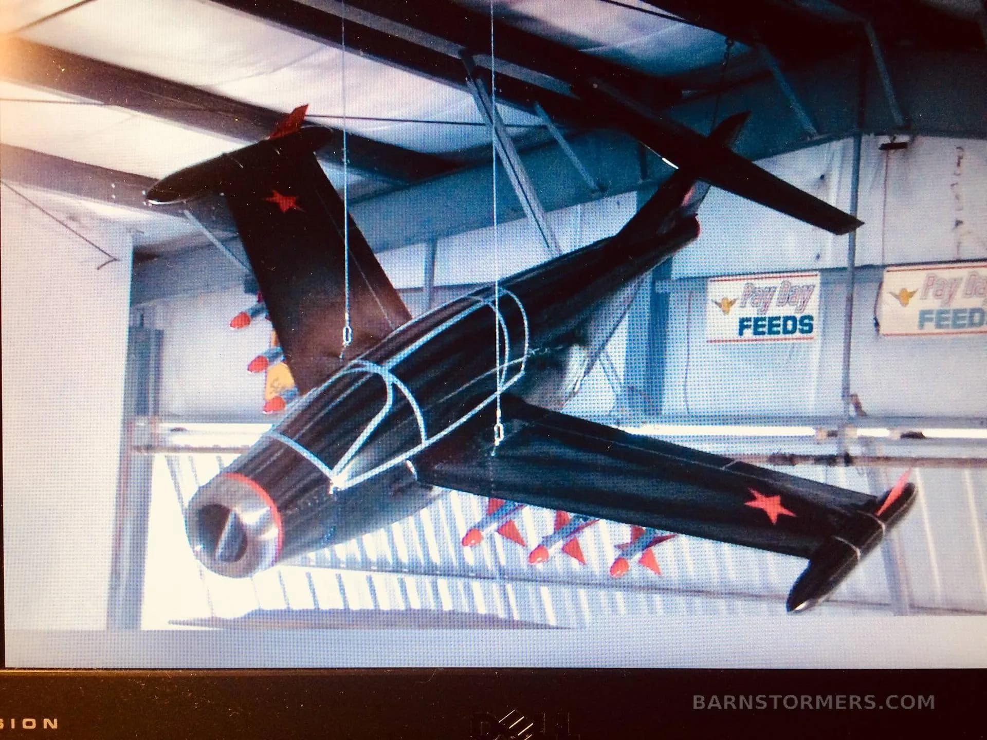 A black model jet aircraft with red stars and missiles, displayed on a screen, hanging in a hangar.