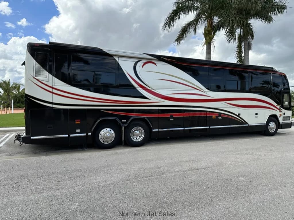 Side view of a Prevost coach with a black, white, and red paint scheme parked outside.