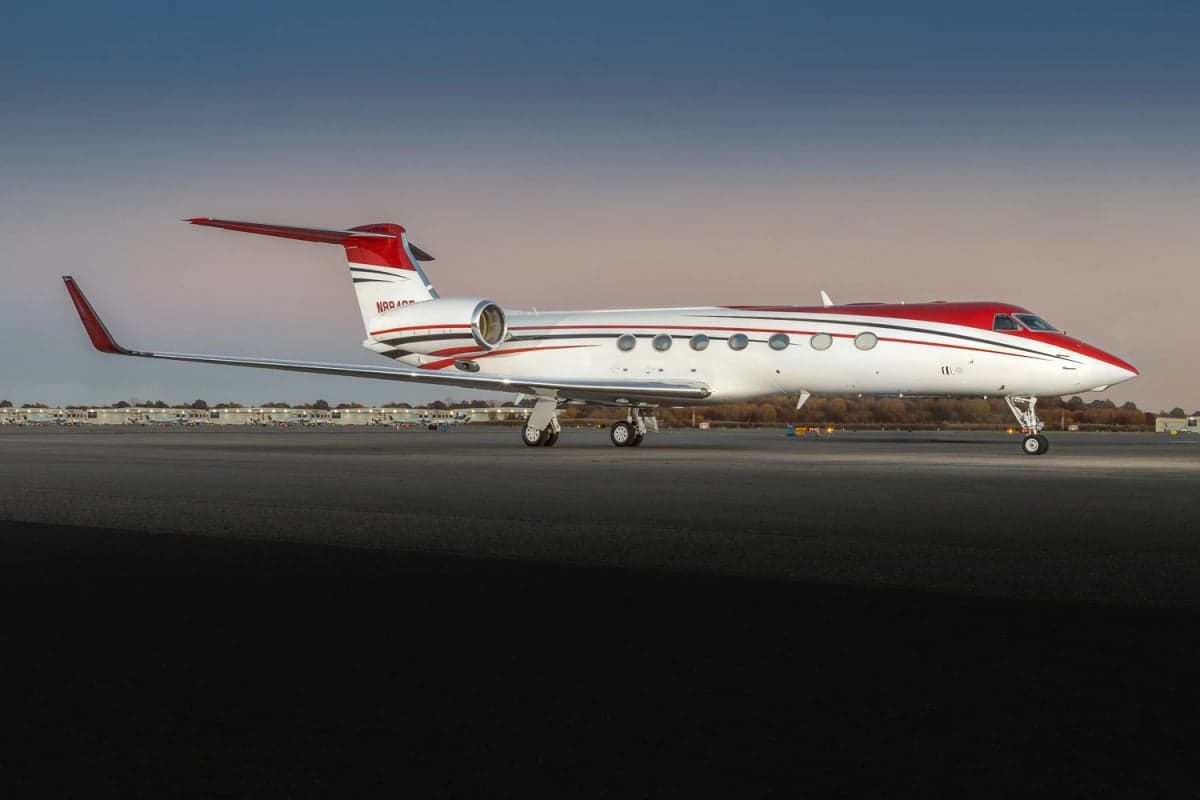 Side view of a red and white Gulfstream G550 on the tarmac.