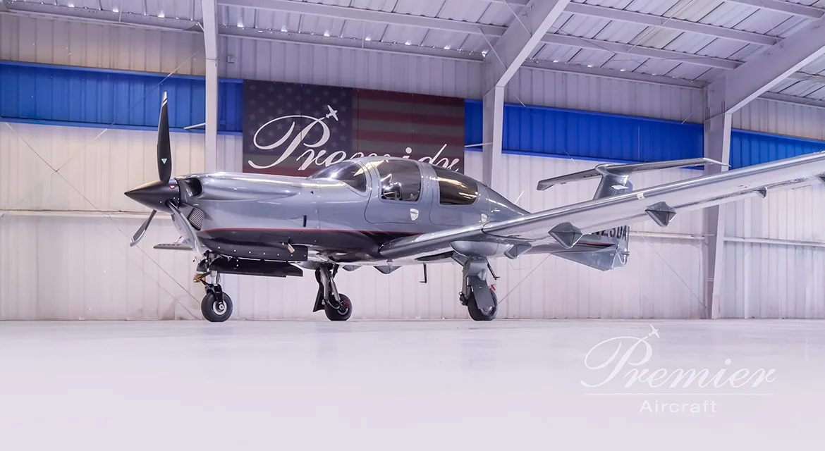 A gray Diamond DA62 aircraft is parked in a hangar with a Premier Aircraft banner in the background.