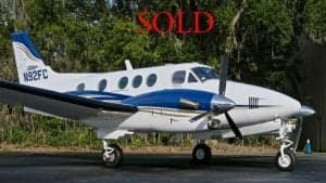A white and blue twin-engine aircraft is parked on the tarmac with the word SOLD overlaid.
