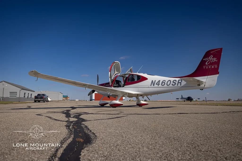 A low-angle view of a white and maroon Cirrus SR22T aircraft, N460SR, with open doors, parked on an airfield.
