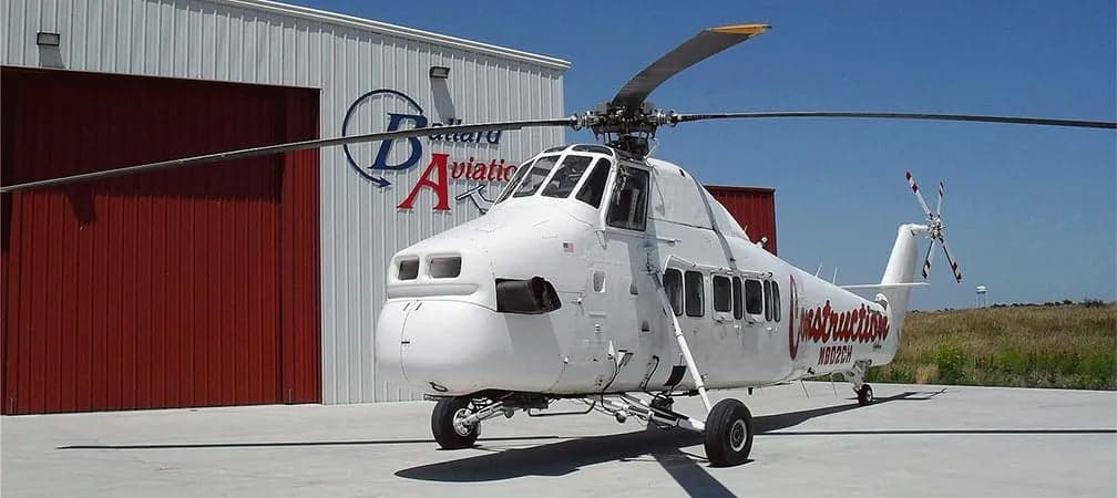 A Sikorsky S-58 helicopter is parked in front of a hangar.