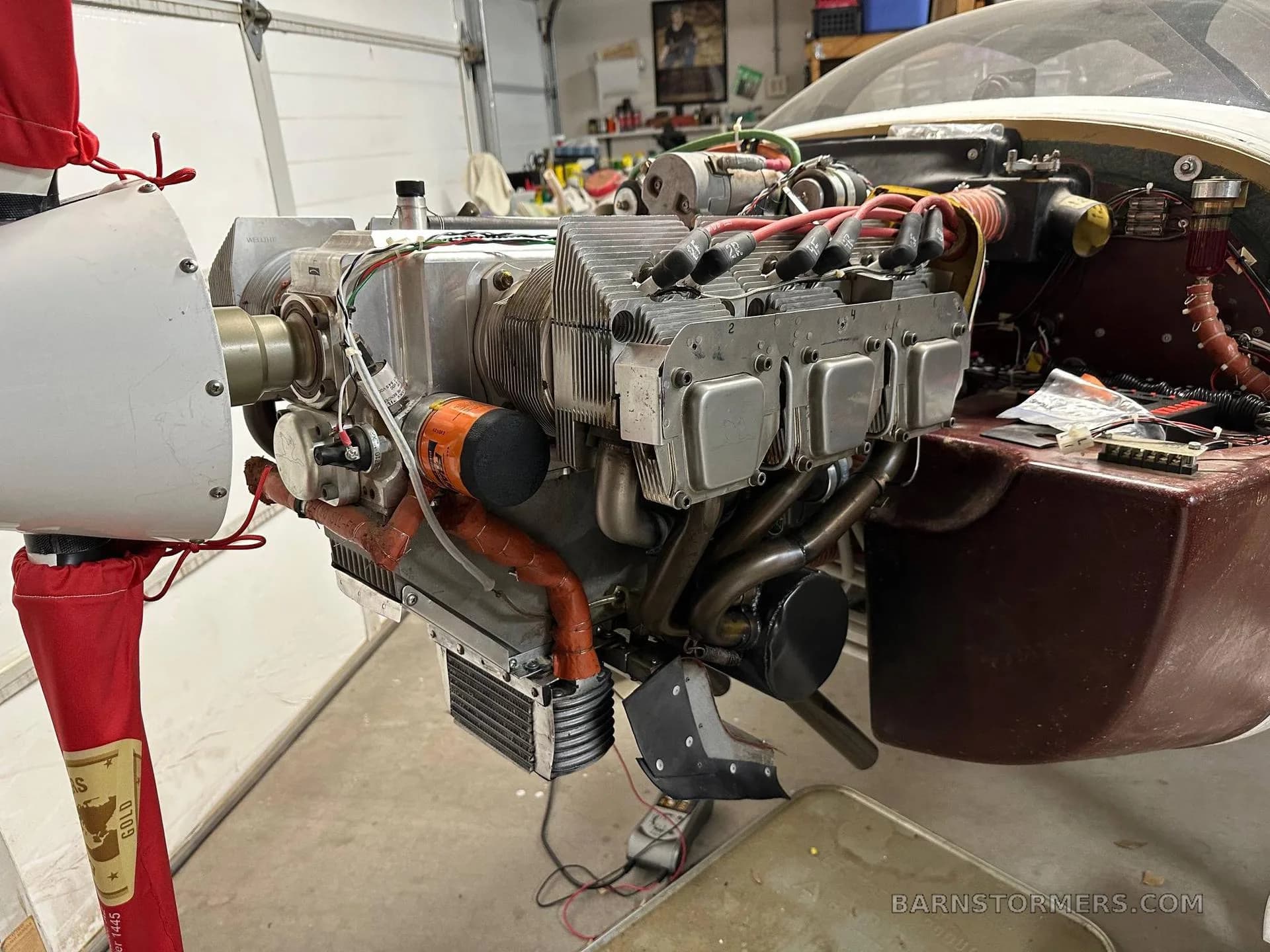 The exposed engine of a light aircraft, showing cylinders, exhaust, and propeller hub, likely in a hangar.