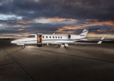 A Learjet 45XR aircraft is parked on the tarmac at dusk with the door open.
