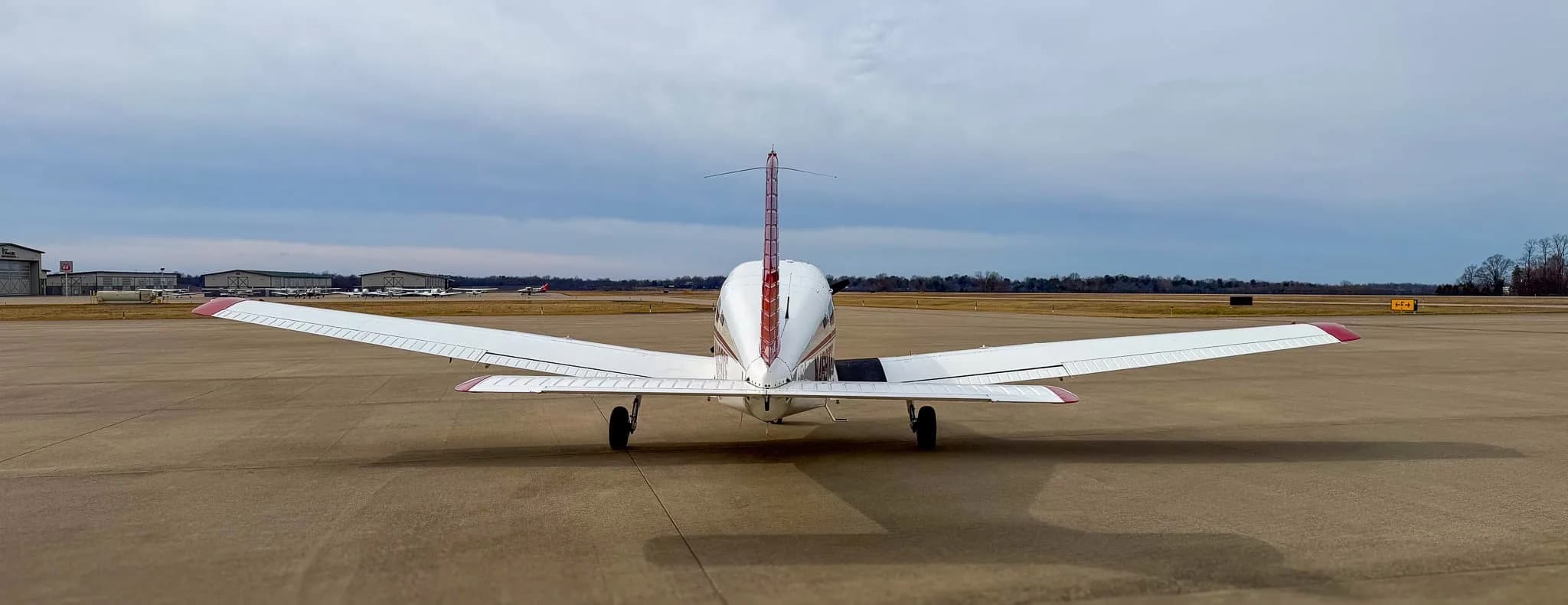 A rear view of a white and red Piper Archer TX aircraft parked on an airfield.
