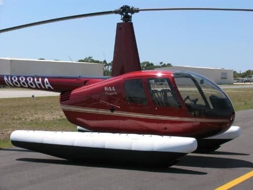 A red Robinson R44 helicopter with floats is parked on the tarmac.