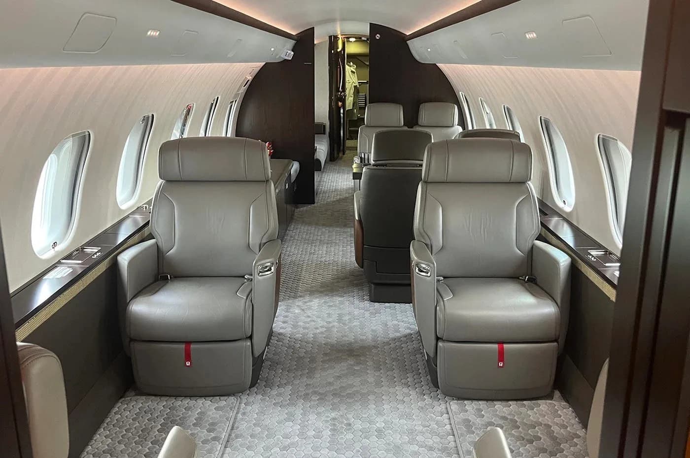 The luxurious cabin interior of a business jet with grey leather seats and a patterned carpet.