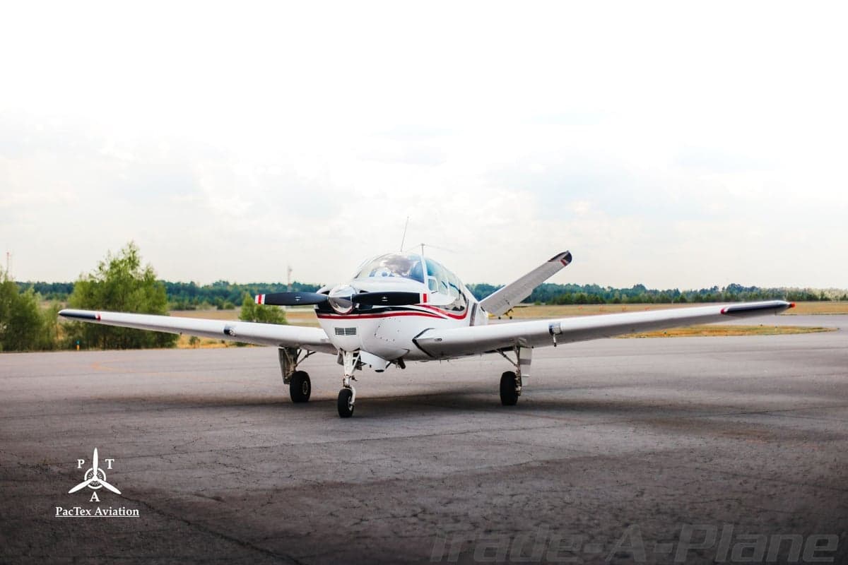 Frontal view of a white single-engine aircraft with red and black stripes parked on an airfield.