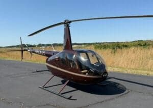A Robinson R44 helicopter with a dark red paint scheme is parked on the tarmac.