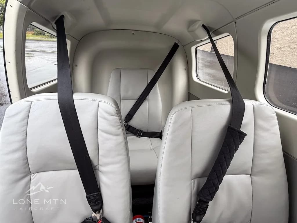 The light gray leather rear seats of the aircraft cabin are visible with seatbelts.