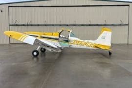 Yellow and white Air Tractor crop duster parked in front of a hangar.
