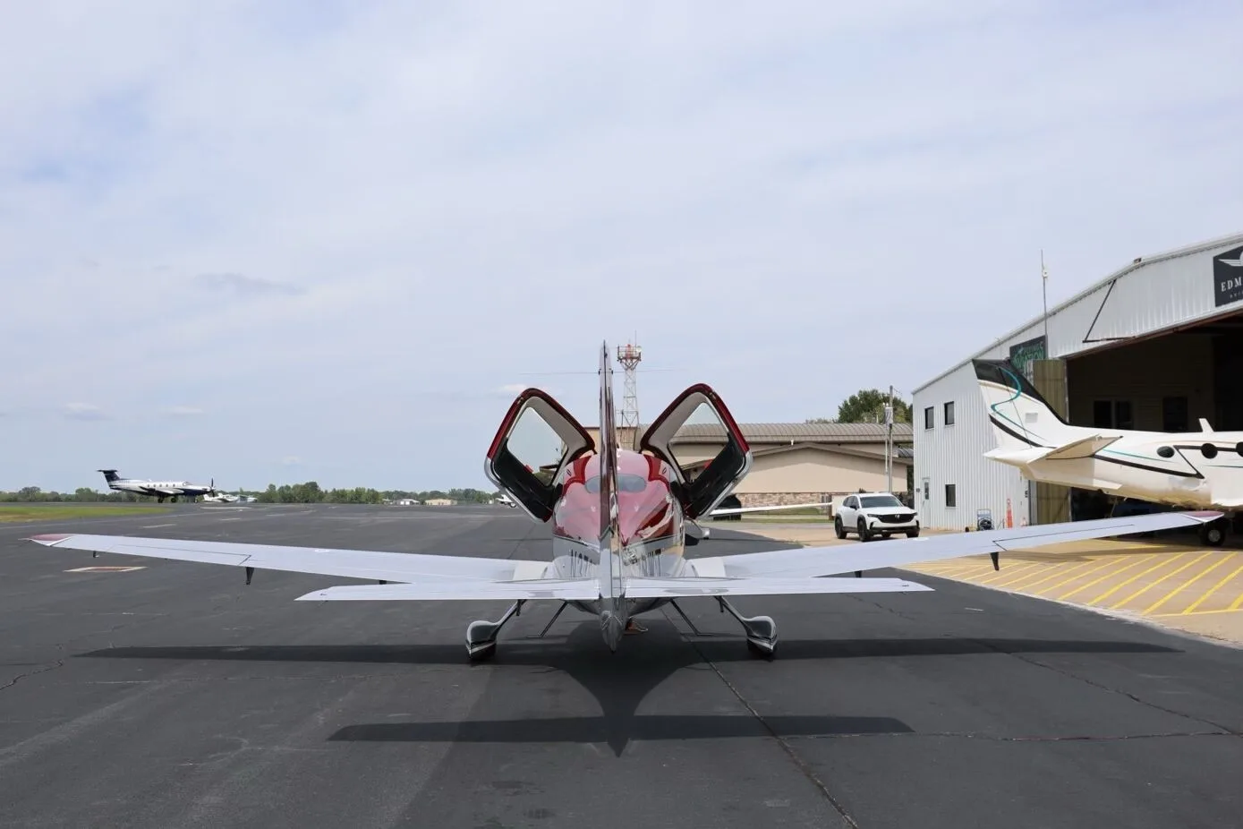 A rear view of the red and silver Cirrus SR22T aircraft with its doors open, parked on an airfield.