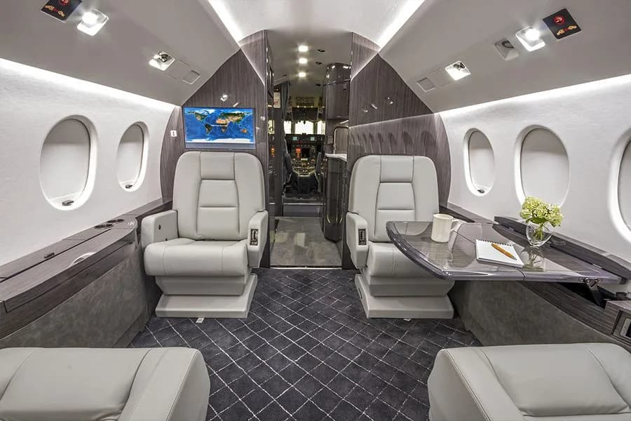The forward cabin of a private jet with two facing seats, a small table, and a map display.