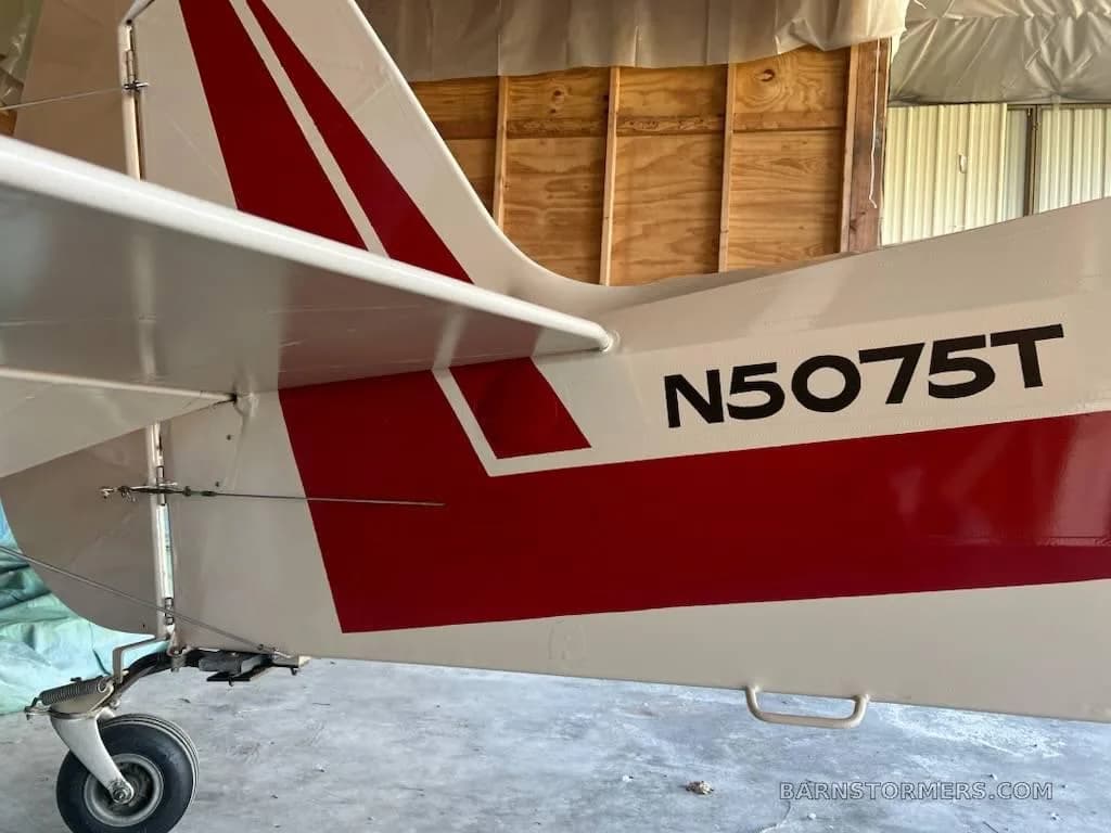 A close-up view of the white and red tail section of aircraft N5075T, showing the tailwheel and part of the fuselage inside a hangar.