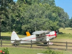 A Howard DGA-15P aircraft is parked in a grassy field near a wooden fence.