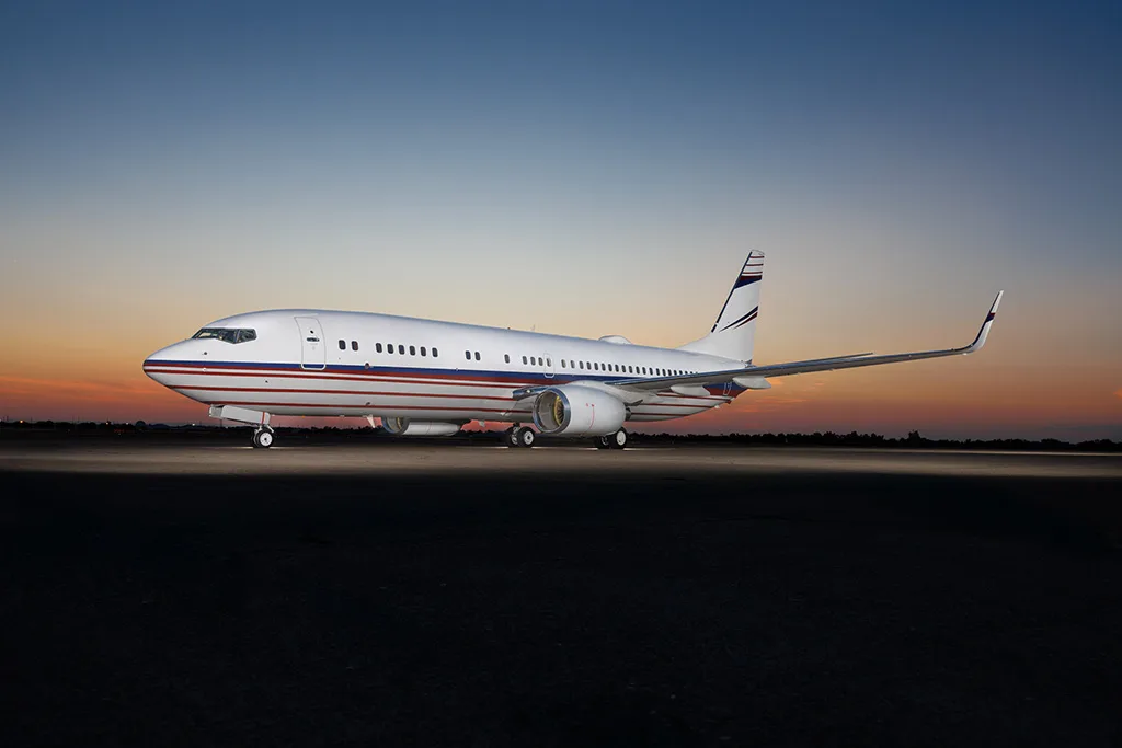 A white Boeing 737 with red and blue stripes on the tarmac at sunset.