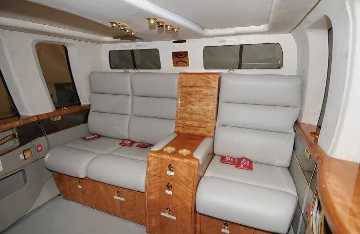 A luxurious helicopter interior with light gray leather seats, wood paneling, and gold accents.