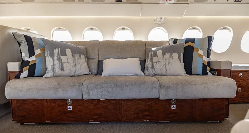A comfortable three-seat divan with decorative pillows inside the cabin of a business jet.