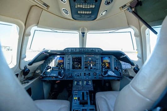 The cockpit of a business jet, featuring multiple display screens and control yokes.