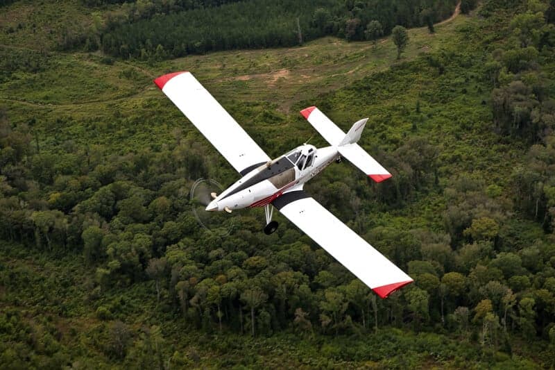 Aerial view of a Thrush 510G crop duster flying over a forest.
