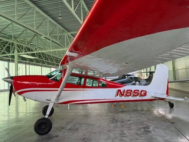 A side view of the red and white Cessna 180/185 aircraft, tail number N8SQ, in a hangar.