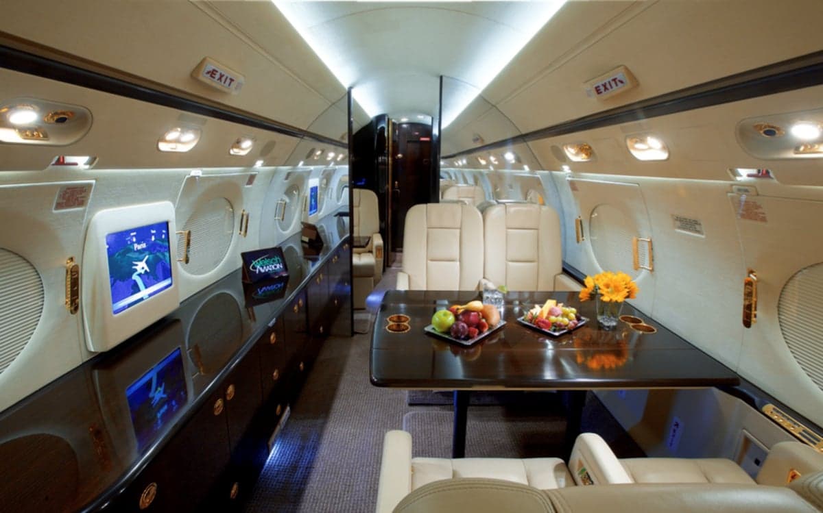 View of the aircraft interior with leather seats, a table, and monitors.