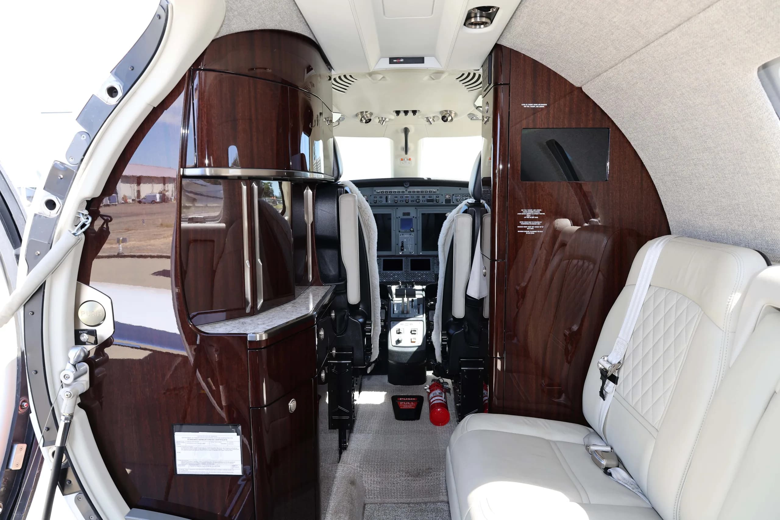 A view from the cabin looking forward into the cockpit, showing a dark wood-paneled galley area and light leather seats.