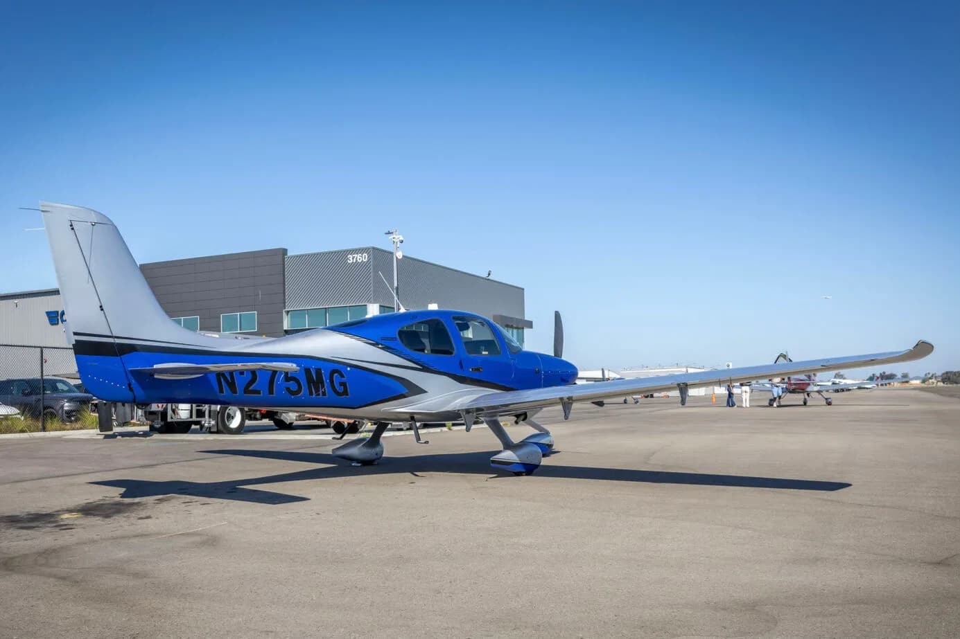 A side view of the blue and silver Cirrus SR22 aircraft, N275MG, parked on an airport tarmac.
